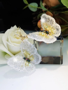 Macro shot of handmade butterfly earrings with crystals and white rose details