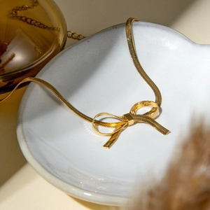 Detail of a gold-plated flat snake chain creatively woven into a bow-knot pendant