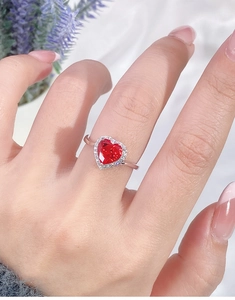 Close-up of a heart-shaped red ruby ring with sparkling diamond halo on woman's finger