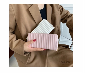 Detail of elegant pleated long PU leather wallets in white and pink held by a model