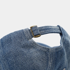 Detail of blue denim baseball cap showing bronze metal buckle and adjustable strap