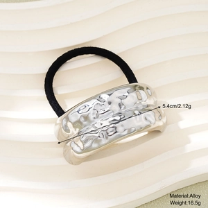 Detail view of silver alloy hair tie with hammered texture on a beige tray