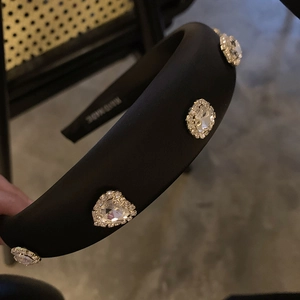 Close-up of black satin padded headband featuring large rhinestones and handmade mark