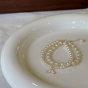 Elegant double-layered pearl bracelet with a golden zircon fishtail charm on ceramic tray