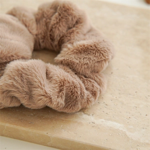 Close-up of soft brown faux fur scrunchie on beige stone surface showing plush texture