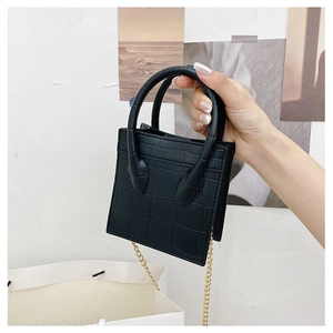 Detail of black crocodile texture mini bag with elegant gold chain strap held by hand