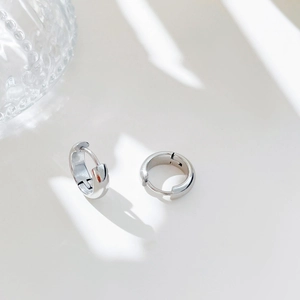 Minimalist silver huggie hoop earrings with a polished mirror finish on white background