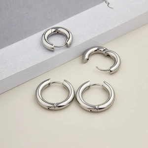 Polished silver hoop earrings shown in both open and closed states on a modern prop