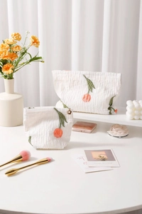 Close-up of white quilted cosmetic bags featuring orange tulip embroidery and flower charms