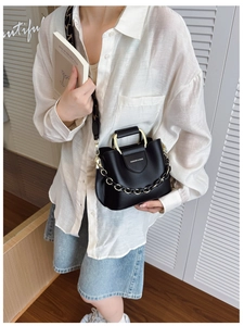 Detail of black leather bucket bag featuring decorative gold chain and patterned wide strap