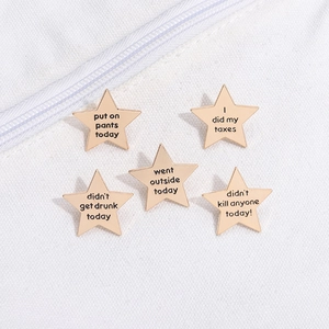 Set of five gold star enamel pins with humorous motivational quotes on white canvas