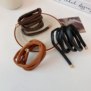 Detail view of leather hair ties in black, dark brown and caramel with gold metal tips