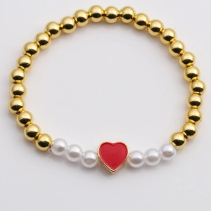 Golden beaded bracelet with white pearls and a red heart pendant on a reflective surface