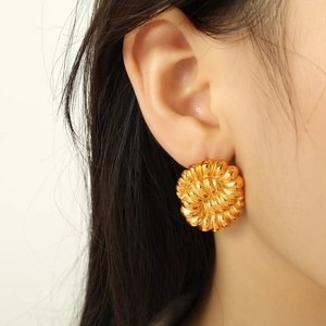 Golden hollow flower earrings with spiral texture shown on a female model's ear
