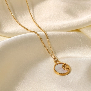 Detail shot of a gold-plated necklace with a white shell pendant on beige silk
