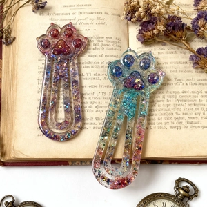 Glittery cat paw resin bookmarks with purple dry flowers on a vintage open book