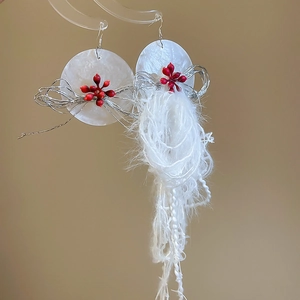 Detailed view of resin flower earrings with silver wire, red beads and white tassels