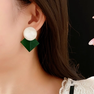 Close-up of white and dark green geometric resin drop earrings worn by a model
