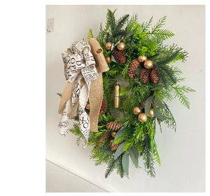 Detail view of a lush Christmas wreath with pine cones, golden bells, and burlap bow