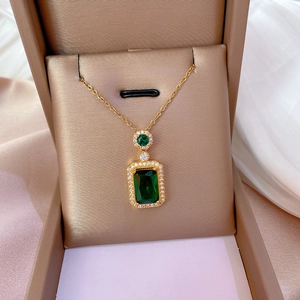 Detail of luxury gold necklace featuring a rectangular green gemstone in a jewelry box