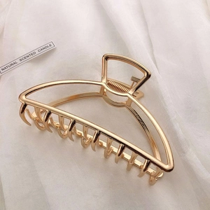 Detail of a large gold metal hair claw clip with geometric cutout design on white fabric