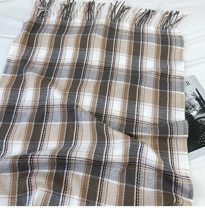Close-up of winter plaid scarf with fringe edge in brown, grey, and beige tones