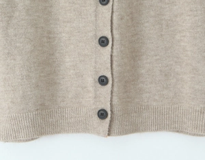 Detailed close-up of knitted cardigan buttons and soft ribbed texture in oatmeal color