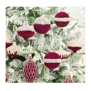 Close-up of luxury flocked wine red Christmas ornaments with gold glitter on snowy tree
