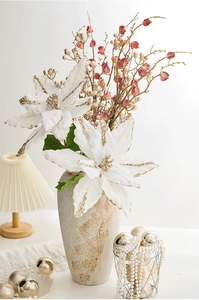 Détail d'un poinsettia artificiel blanc avec bords dorés et baies dans un vase en céramique