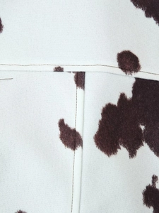 Close-up of brown and white cow print jacket fabric showing detailed stitching and texture