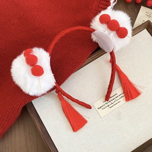 Detail of red festive headband featuring white plush pom-poms and long tassels
