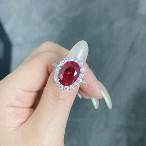 Detailed view of an oval red gemstone ring with a halo of clear stones on a silver band