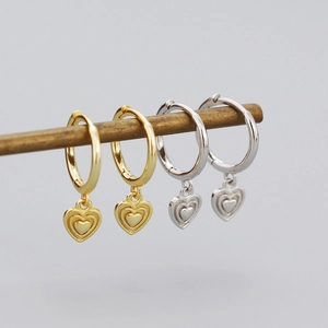 Detailed view of gold and silver heart-shaped hoop earrings on minimalist display