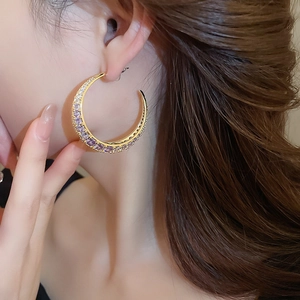 Close-up of model wearing gold-plated crescent earrings with purple and white stones