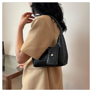 Detailed view of black woven shoulder bag with small coin purse on a model's shoulder