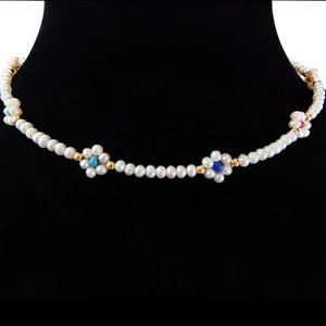 Detailed view of baroque pearl choker with colorful flower charms on a black display stand