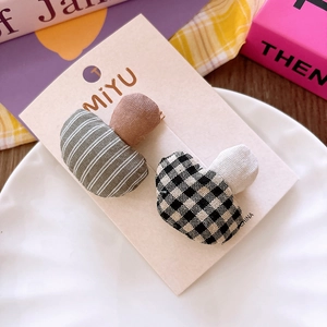 Detail of two mushroom-shaped fabric hair clips in plaid and stripe patterns for girls