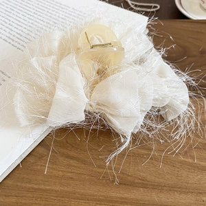Détail de la pince à cheveux blanc crème avec nœud en tissu à franges et décor de livre