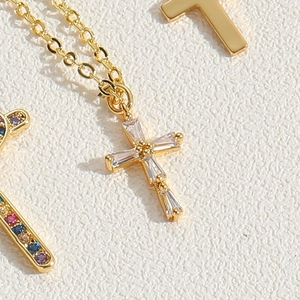 Detailed macro view of a gold cross pendant necklace with baguette-cut zircon inlays