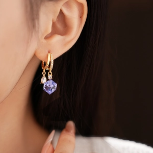 Close-up of golden drop earrings with purple zircon crystals worn by a model