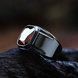 Macro shot of men's vintage stainless steel ring with a faceted red stone on charcoal wood