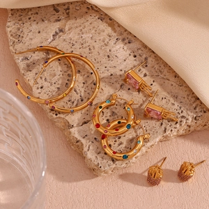 Detail of 18K gold plated earrings featuring colorful zirconia stones on a stone surface