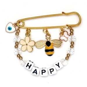 Detail of a golden safety pin brooch featuring a blue evil eye heart and HAPPY letter beads