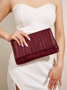 Dettaglio ravvicinato della borsa da sera plissettata rosso scuro tenuta da una modella