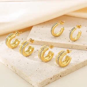 Close-up of three gold C-shaped hoop earrings with inlaid zircons on a stone tray