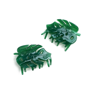 Close-up of dual green acetate hair claws in monstera leaf design on white background