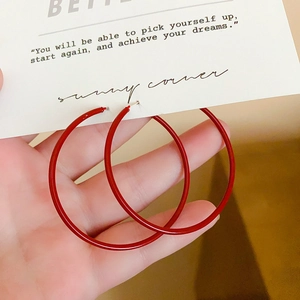 Macro view of minimalist large bright red glossy hoop earrings held on a white display card