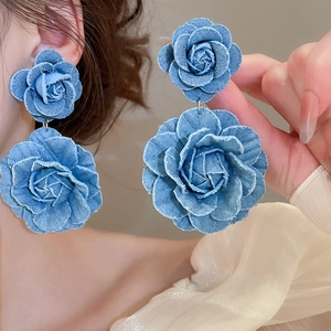 Detailed close-up of denim blue fabric rose earrings on a model with frayed edges