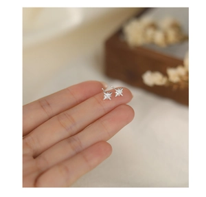 Close-up of mini S999 sterling silver star stud earrings held by hand over a jewelry box