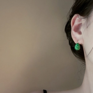 Close-up of emerald green teardrop earrings with elegant gold hooks on model's profile